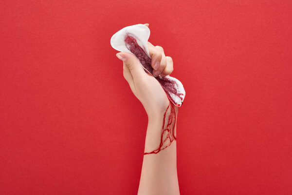 partial view of woman squeezing sanitary towel with blood on red background