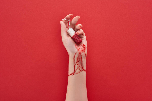 частичный вид женщины, держащей тампон с кровью на красном фоне
