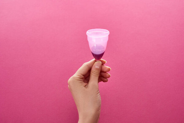 частичный вид женщины, держащей менструальную чашку с кровью на фиолетовом фоне
