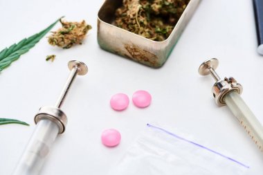 close up view of marijuana buds, syringes near pink ecstasy and heroin on white background clipart