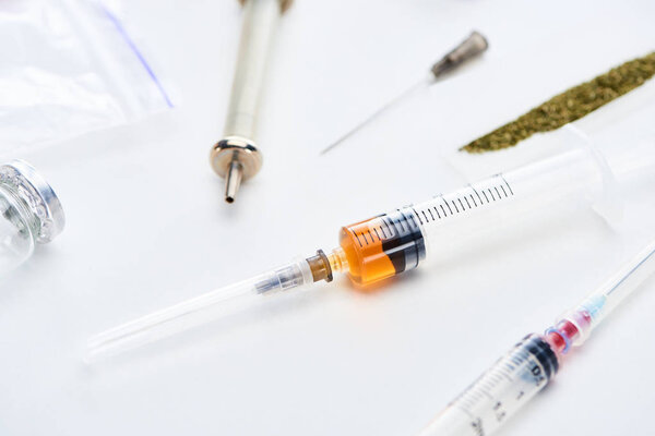 close up view of ampoule, syringes, heroin and hemp on white background
