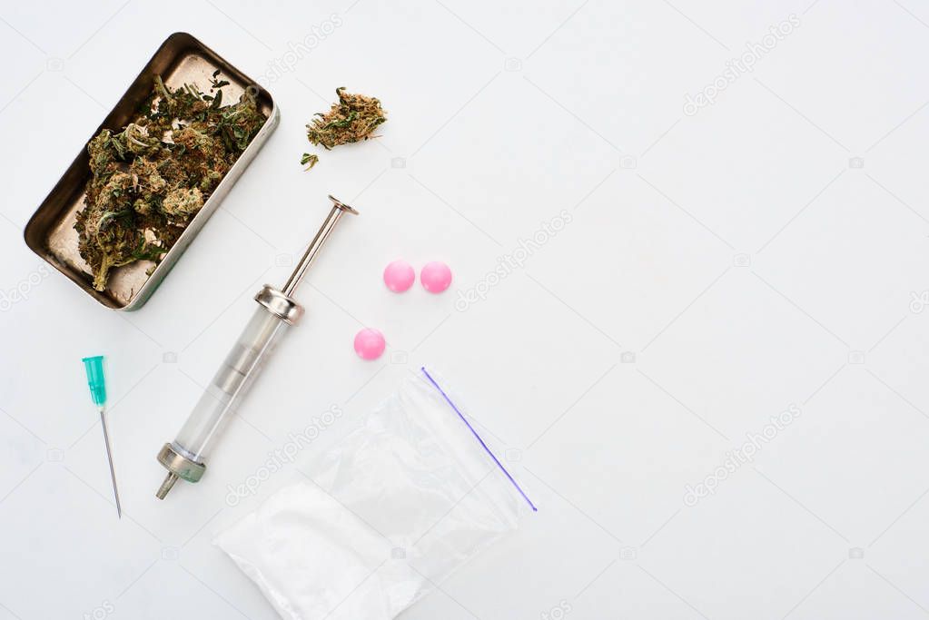 top view of marijuana buds, heroin, lsd and syringe on white background