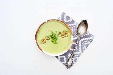 top view of delicious creamy green vegetable soup with sprouts and pumpkin seeds on napkin with spoon isolated on white clipart