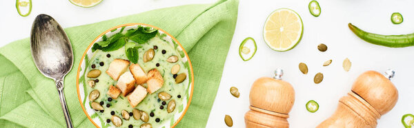 top view of delicious creamy green vegetable soup near pepper and salt mills and scattered ingredients isolated on white, panoramic shot