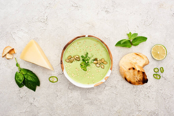 top view of tasty green creamy soup with croutons, cheese and spinach on textured grey background