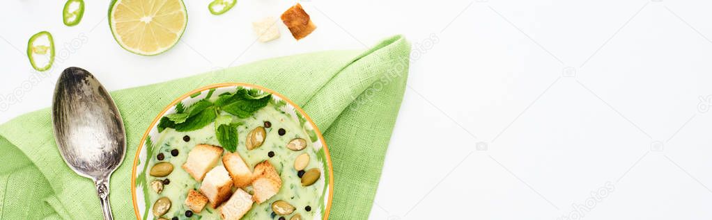 top view of delicious creamy green vegetable soup with pumpkin seeds . mint and croutons served isolated on white, panoramic shot