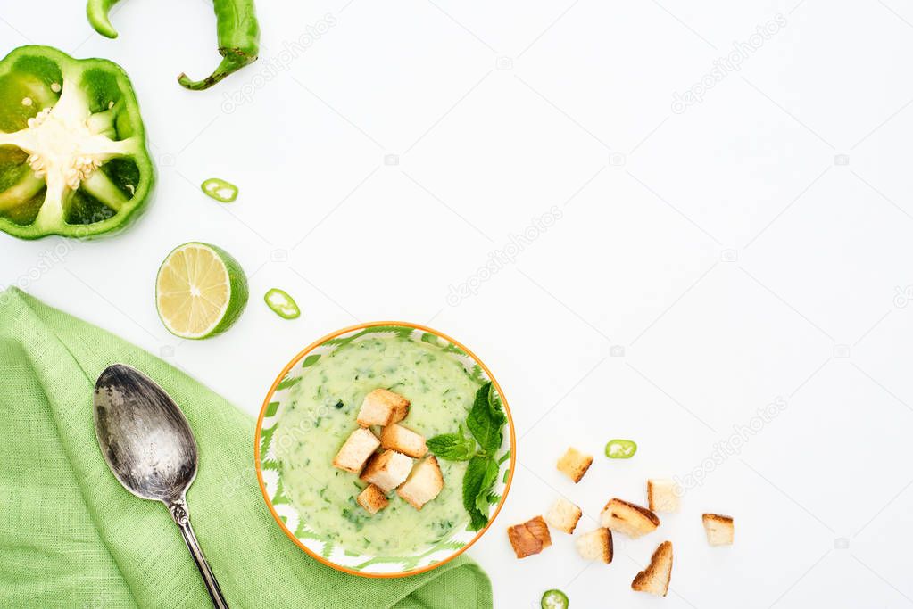 top view of delicious creamy green vegetable soup served with napkin and spoon isolated on white