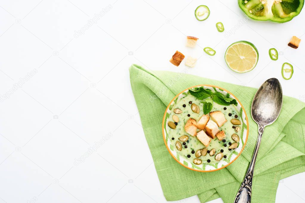 top view of delicious creamy green vegetable soup served on napkin near spoon isolated on white