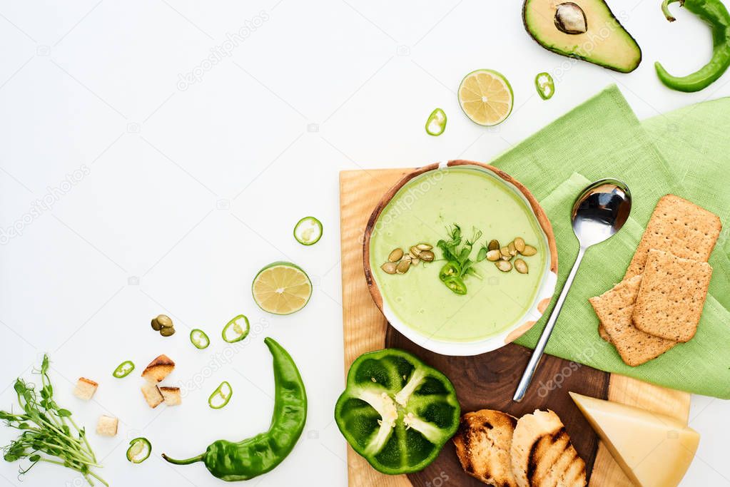 top view of delicious creamy green vegetable soup served with croutons ans crackers isolated on white