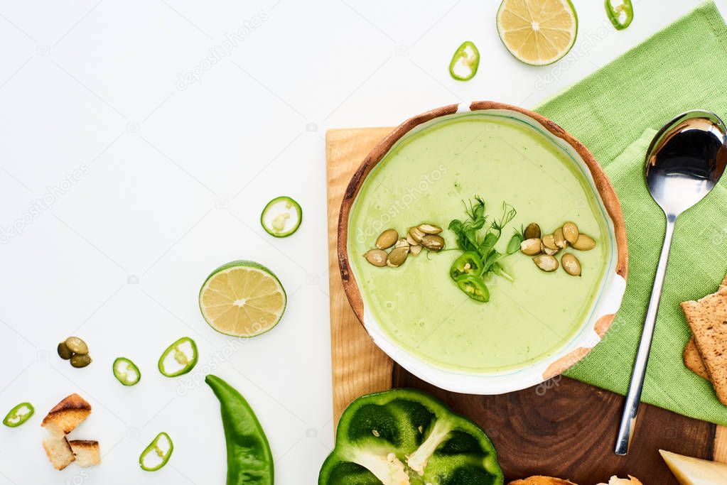 top view of delicious creamy green vegetable soup served on wooden board isolated on white