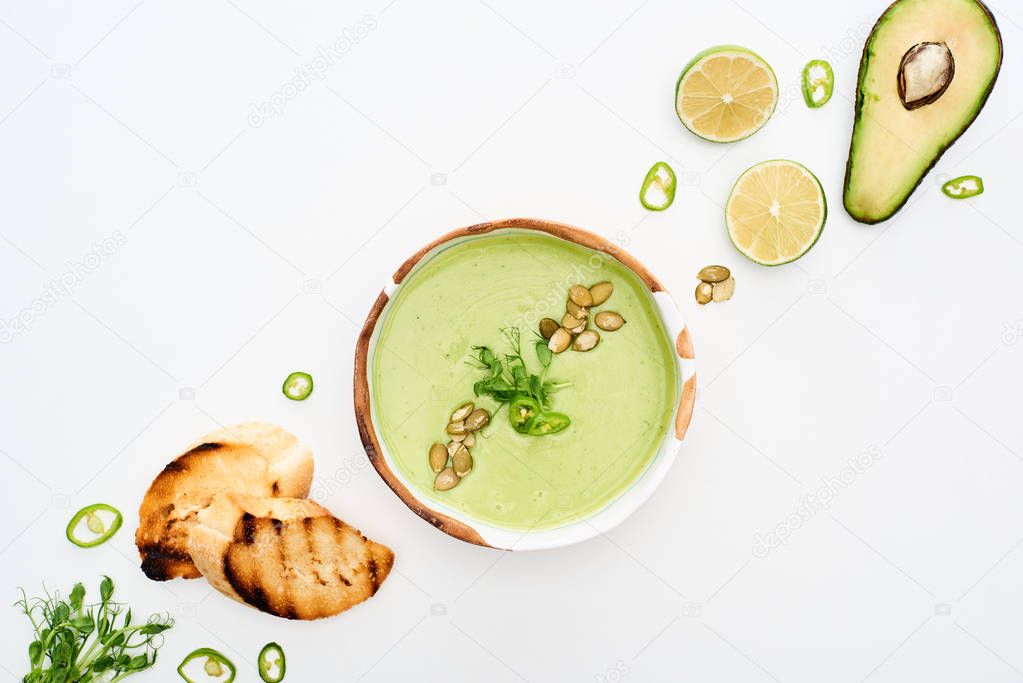 top view of delicious creamy green vegetable soup with lime and croutons isolated on white