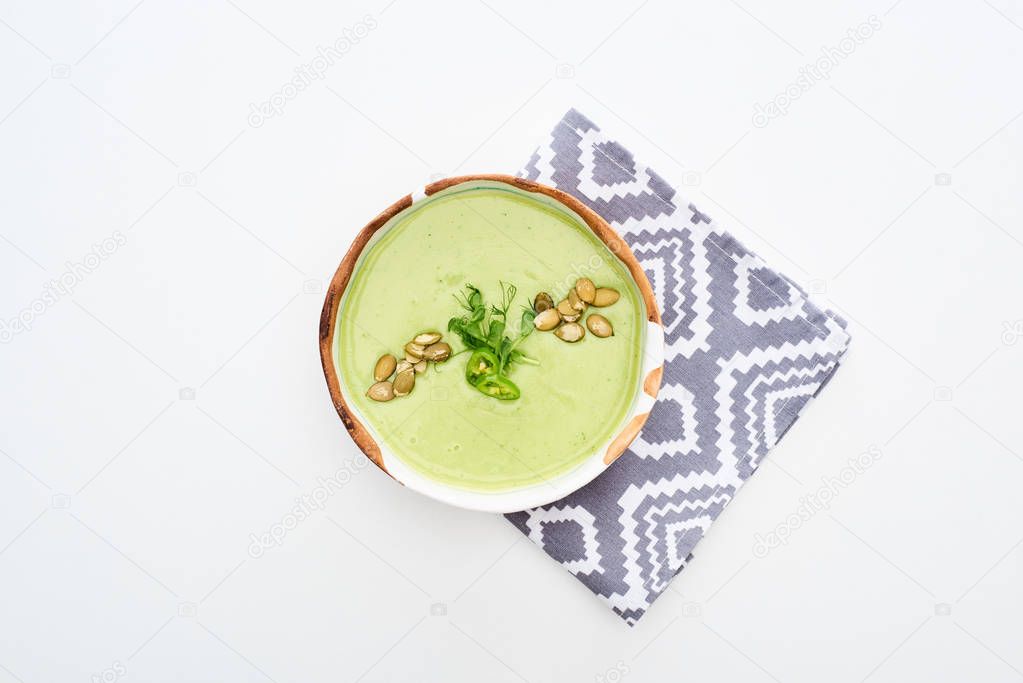 top view of delicious creamy green vegetable soup with sprouts and pumpkin seeds on napkin isolated on white
