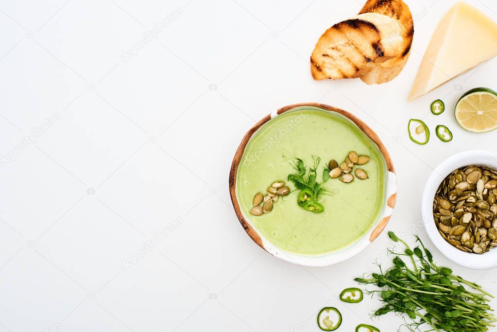 top view of delicious creamy green vegetable soup with sprouts, grilled croutons and pumpkin seeds isolated on white