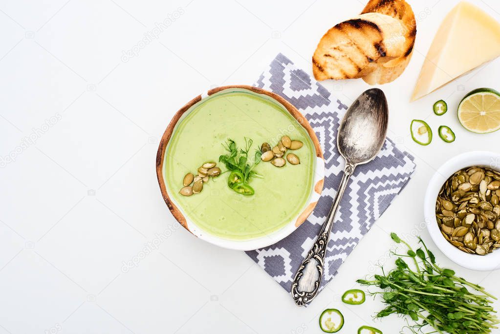 top view of delicious creamy green vegetable soup with sprouts, grilled croutons and pumpkin seeds served on napkin isolated on white