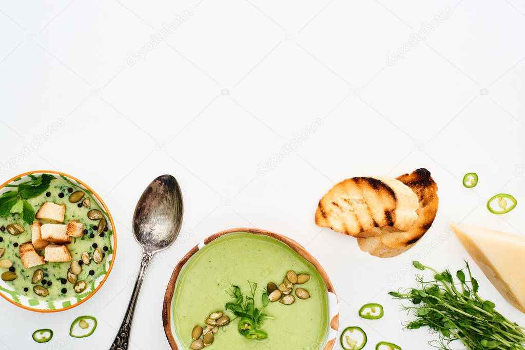 top view of delicious creamy green vegetable soup with sprouts, grilled croutons and cheese isolated on white
