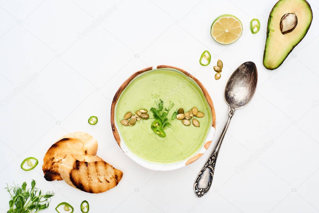 top view of delicious creamy green vegetable soup with lime and croutons near silver spoon isolated on white