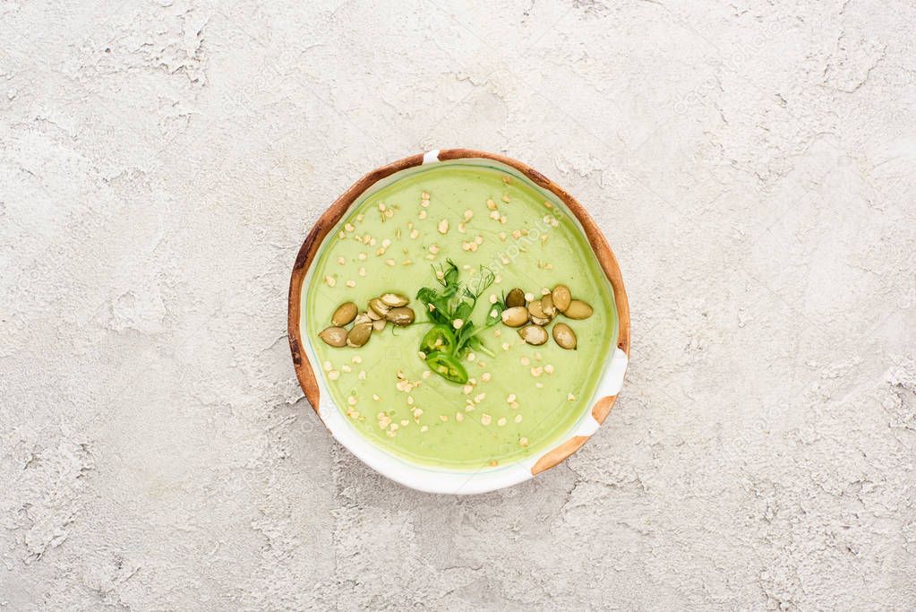 top view of tasty green creamy soup with pumpkin seeds on textured grey background with rustic cloth