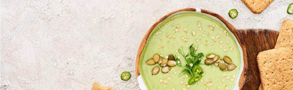 top view of tasty green creamy soup with crackers on wooden chopping board, panoramic shot