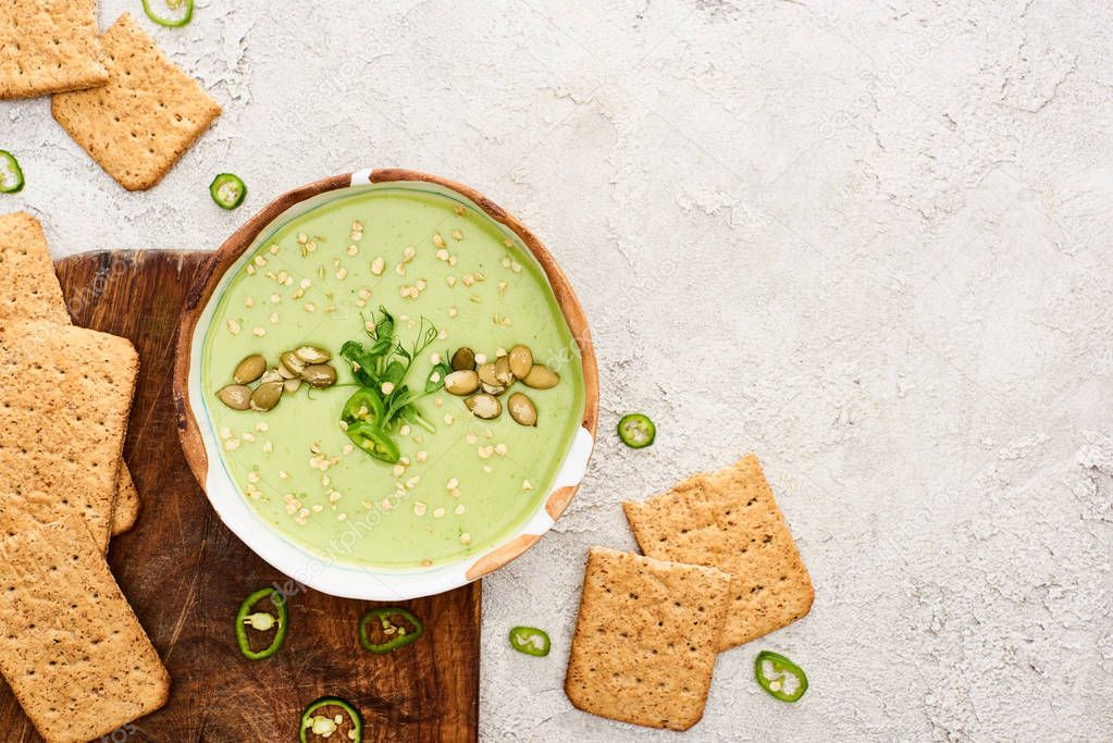 top view of tasty green creamy soup with crackers on wooden chopping board