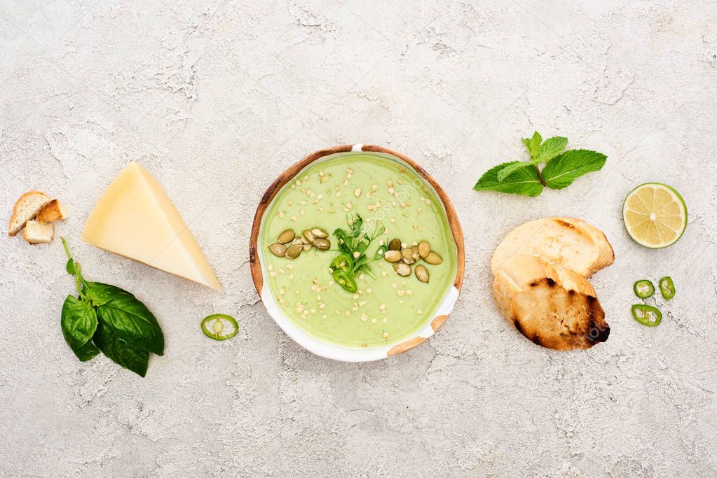 top view of tasty green creamy soup with croutons, cheese and spinach on textured grey background