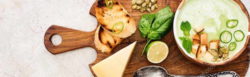 Panoramic shot of green vegetable creamy soup on wooden chopping board near cheese and spoon on textured surface — Stock Image Panoramic Shot Green Vegetable Creamy Soup Wooden Chopping Board Cheese Stock Photo