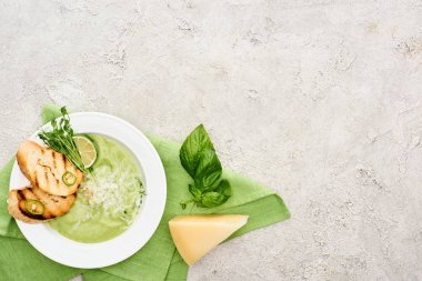top view of delicious creamy green vegetable soup with croutons served on napkin near spinach leaves and cheese clipart