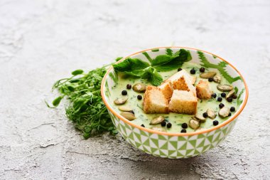 bowl of delicious green vegetable creamy soup with croutons, black pepper and pumpkin seeds near green sprouts clipart