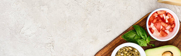 top view of pumpkin seeds, avocado, mint and tomatoes on wooden chopping board, panoramic shot