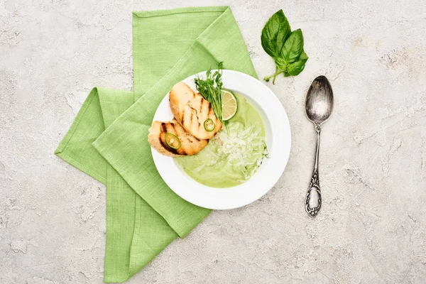 ナプキンとスプーンを添えたクルトンのおいしいクリーミーな緑色の野菜スープのトップビュー — ストック写真
