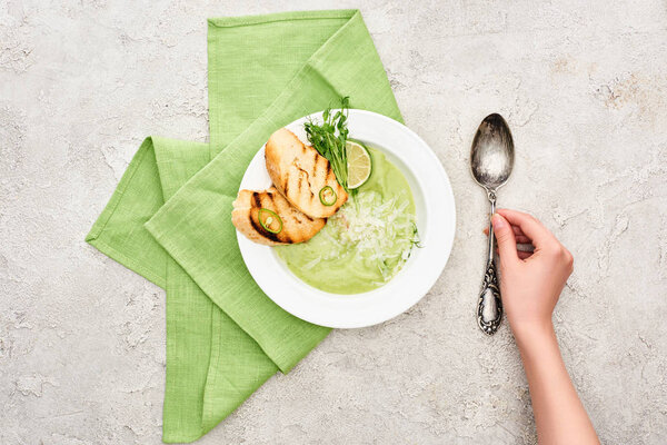partial view of woman putting spoon near delicious creamy green vegetable soup served with croutons