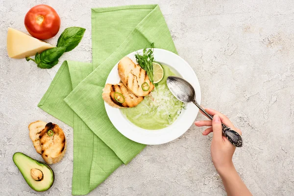 おいしいクリーミーな緑の野菜スープとクルトンとプレートの近くにスプーンを保持している女性のトリミングビュー — ストック写真