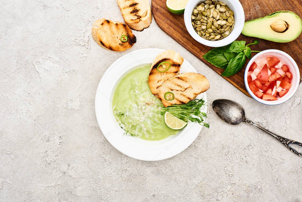 top view of green creamy soup near wooden cutting board with fresh ingredients