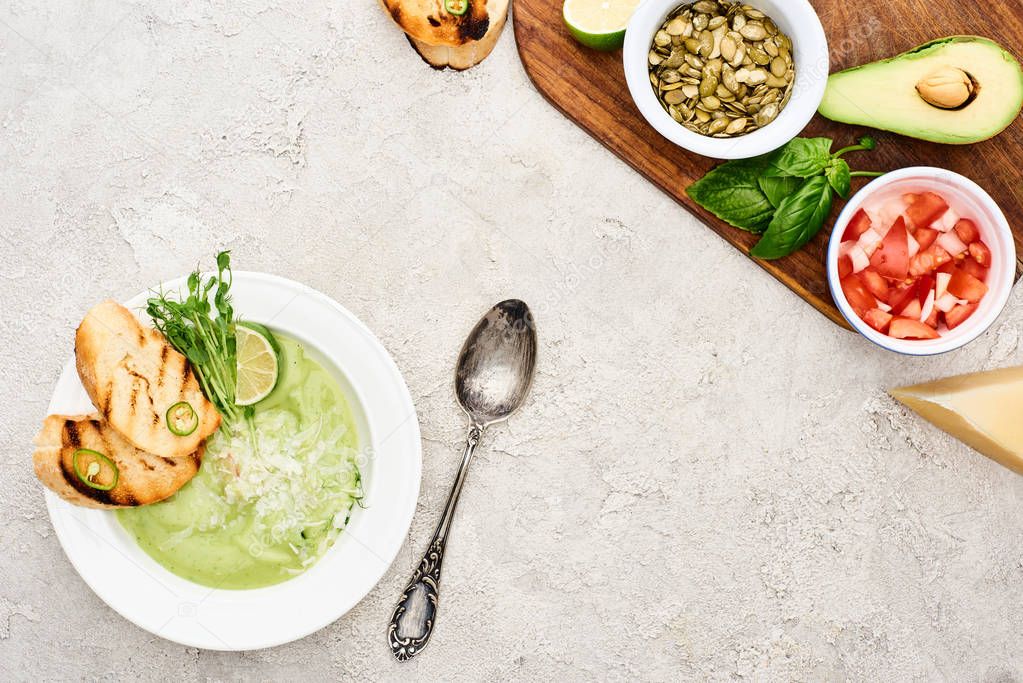 top view of green creamy soup near wooden cutting board with fresh ingredients