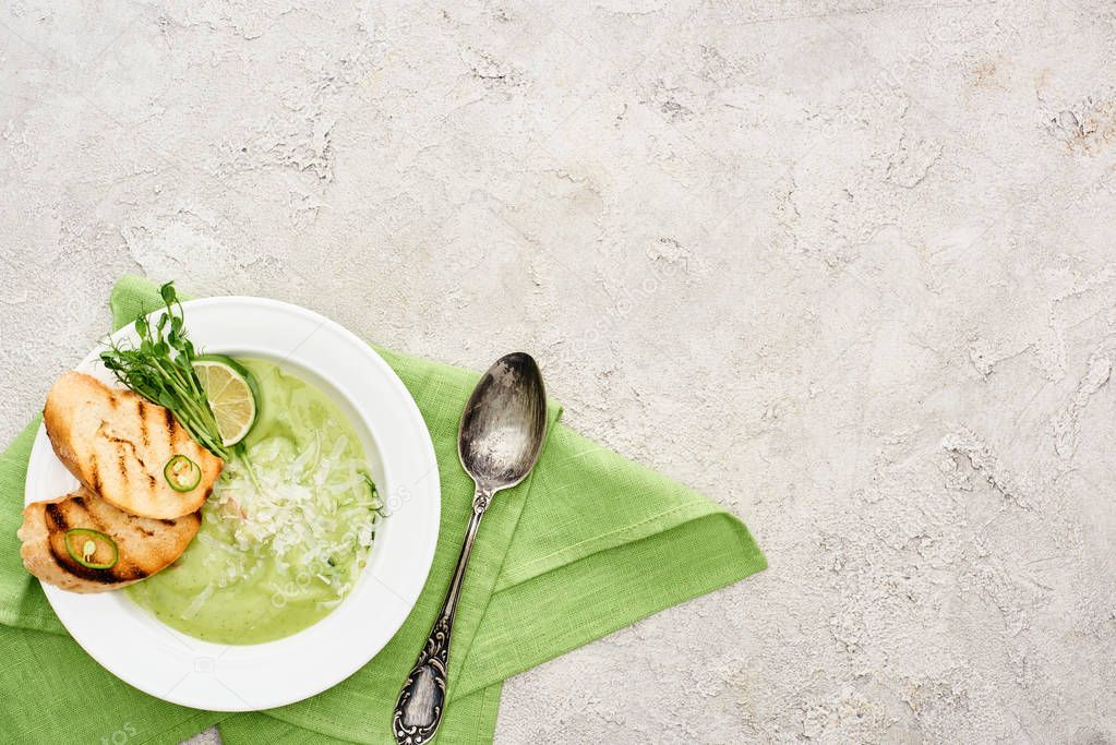 top view of delicious creamy green vegetable soup with croutons served with spoon and green napkin