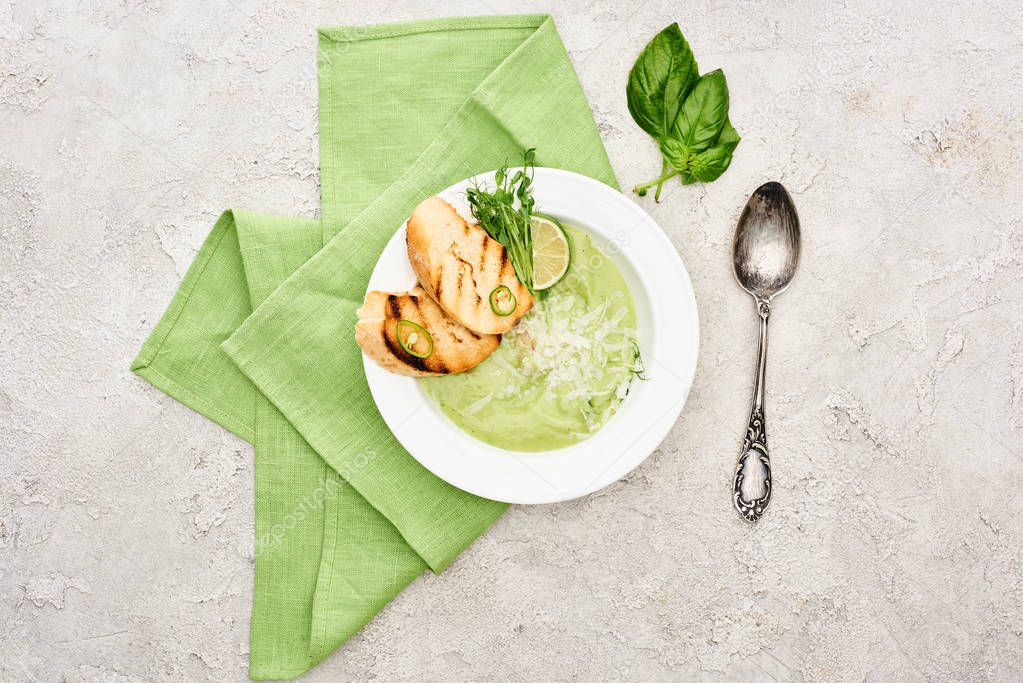 top view of delicious creamy green vegetable soup with croutons served with napkin and spoon
