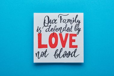 top view of card with our family is defended by love not blood lettering on blue background clipart