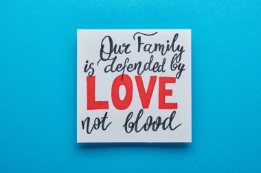 top view of card with our family is defended by love not blood lettering on blue background clipart