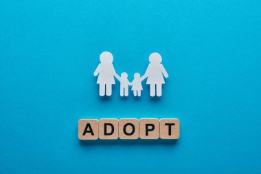 top view of paper cut lesbian family holding hands on blue background with adopt lettering on wooden cubes clipart