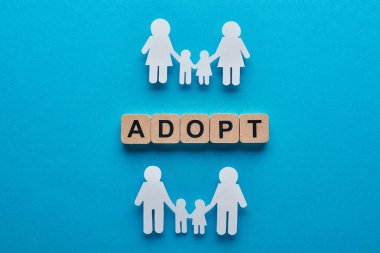 top view of paper cut gay and lesbian families holding hands on blue background with adopt lettering on wooden cubes clipart