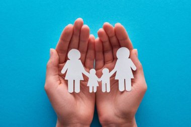 cropped view of woman holding paper cut lesbian family near on blue background clipart