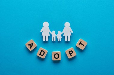top view of paper cut lesbian family holding hands on blue background with adopt lettering on cubes clipart