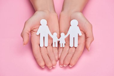 cropped view of woman holding paper cut gay family on pink background clipart