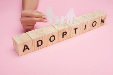pembe arka plan üzerinde evlat edinme yazı ile ahşap küpler üzerinde kağıt kesim gay aile tutan kadın kırpılmış görünümü