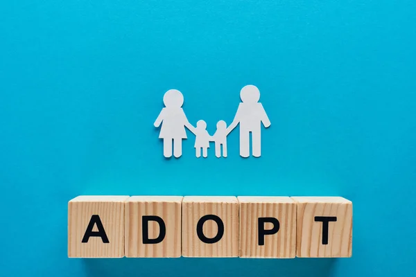 stock image top view of paper cut family holding hands on blue background with adopt lettering on wooden cubes