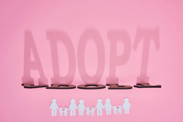 shadow of word adopt and paper cut families on pink background