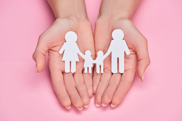 cropped view of woman holding paper cut family on pink background