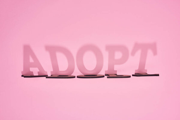 shadow of cardboard word adopt on pink background