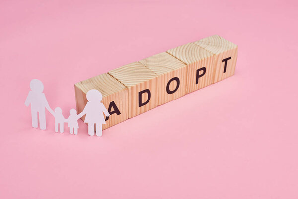 wooden cubes with adopt lettering and paper cut family on pink background