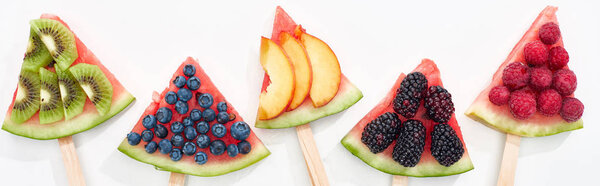panoramic shot of fresh watermelon on sticks with seasonal berries and fruits on white background