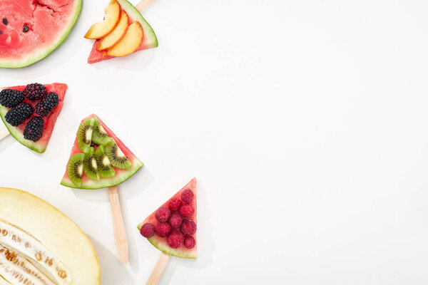 top view of watermelon on sticks with seasonal berries and fruits on white background with copy space